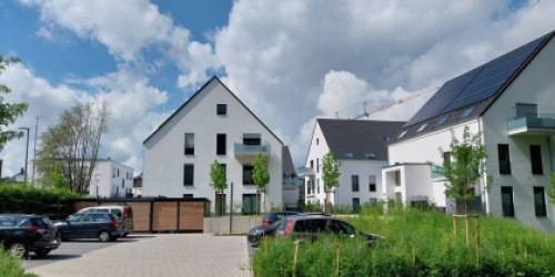 Drei weiße, neue Häuser eines Wohnquartiers mit Parkplätzen und Fahrradabstellanlage davor